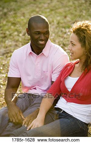 Stock Photo - Close-up of smiling young multi-ethnic couple sitting on grass outdoors. Fotosearch
