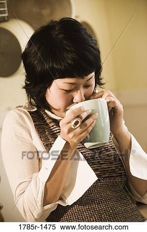 Stock Photography - Close-up of young Asian woman drinking from a cup. Fotosearch