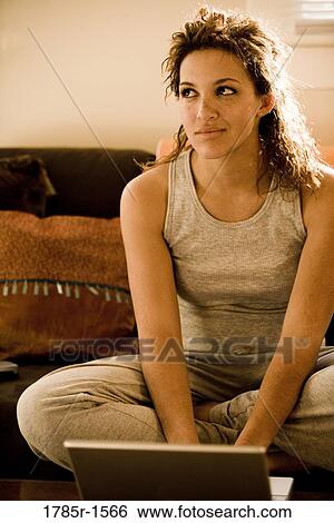 Stock Photograph - Close-up of young woman sitting on sofa using a laptop computer. Fotosearch