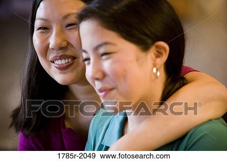 Stock Photo - Close-up portrait of an Asian mother embracing her Asian-Caucasian daughter in the kitchen. Fotosearch