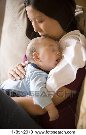 Stock Image - Close-up view of an infant boy falling asleep while being held by his mother. Fotosearch