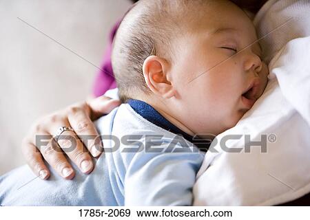 Stock Photo - Close-up view of an infant boy falling asleep while being held by his mother. Fotosearch