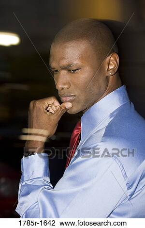 Stock Image - Contemplative young businessman looking away amidst streaks of light in background. Fotosearch