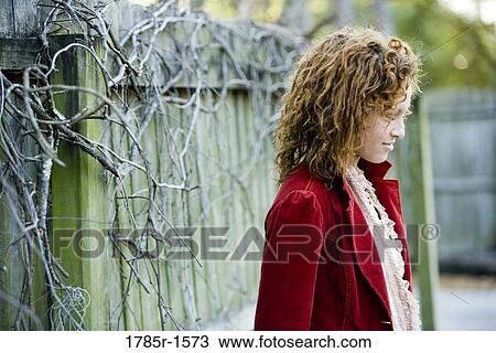 Stock Image - Contemplative young woman standing by a wooden fence. Fotosearch