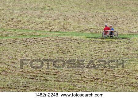 Stock Photo - Couple sitting on a bench in a field, Orcas Island, San Juan Islands, Washington State, USA. Fotosearch