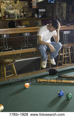 Depressed man in jeans and t-shirt sitting beside billiards table View Large Photo Image Stock Photo - Depressed man in jeans and t-shirt sitting beside billiards table. Fotosearch