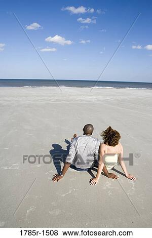 Elevated view of a romantic young couple sitting on beach View Large Photo Image Stock Photo - Elevated view of a romantic young couple sitting on beach. Fotosearch