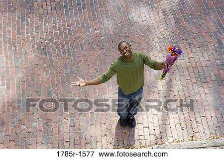 Stock Photo - Elevated view of a young man on street with bouquet of flowers. Fotosearch