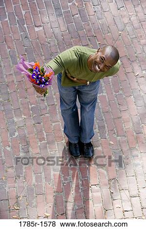 Stock Photo - Elevated view of a young man on street, bowing and gesturing upwards with bouquet of flowers. Fotosearch