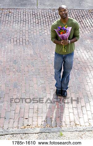 Elevated view of a young man standing on street looking hopeful while holding bouquet of flowers View Large Photo Image Stock Image - Elevated view of a young man standing on street looking hopeful while holding bouquet of flowers. Fotosearch