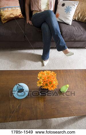 Elevated view of flowers in a vase on coffee table with woman's legs on sofa in background View Large Photo Image Stock Photo - Elevated view of flowers in a vase on coffee table with woman's legs on sofa in background. Fotosearch