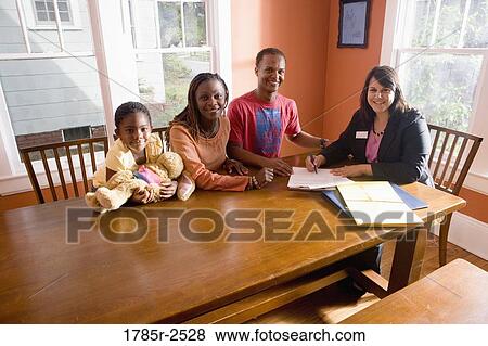 Stock Photo - Family at home signing papers with agent. Fotosearch