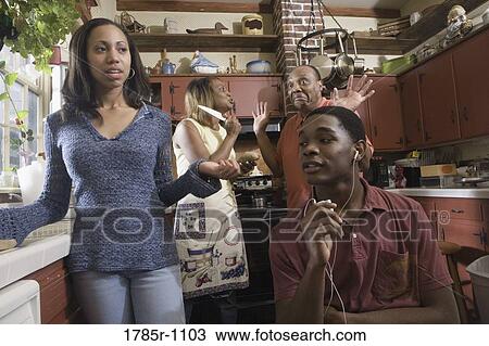 Stock Image - Family conversing in kitchen while son listens to headphones. Fotosearch