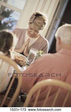 Stock Image - Family sitting at the dining table praying. Fotosearch