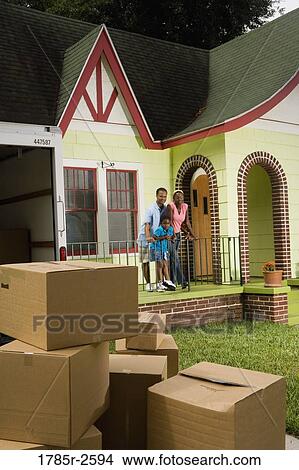 Picture - Family standing outside house, with moving boxes piled in driveway. Fotosearch
