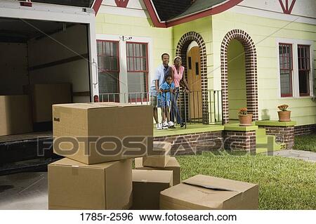 Stock Photograph - Family standing outside house, with moving boxes piled in driveway. Fotosearch