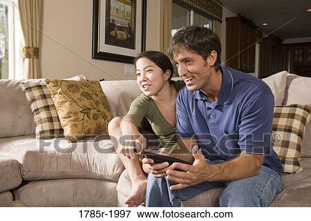 Stock Photo - Father and daughter on sofa watching TV. Fotosearch