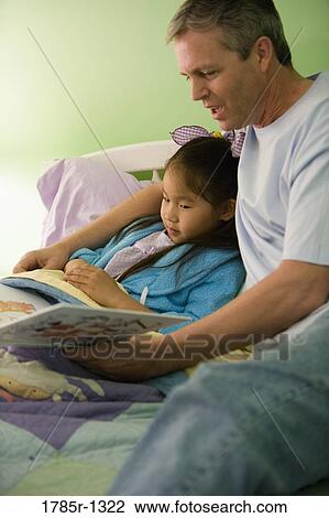 Stock Image - Father and daughter reading book in bedroom. Fotosearch