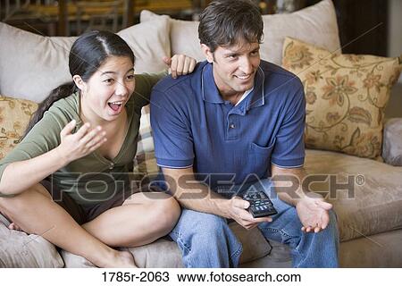 Stock Image - Father and daughter watching TV from sofa. Fotosearch