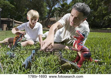 Father and son playing with toy dinosaurs on grassy lawn View Large Photo Image Stock Image - Father and son playing with toy dinosaurs on grassy lawn. Fotosearch