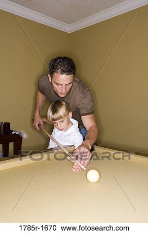 Stock Image - Father showing his young son how to play pool. Fotosearch
