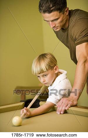 Stock Photo - Father showing his young son how to shoot pool. Fotosearch