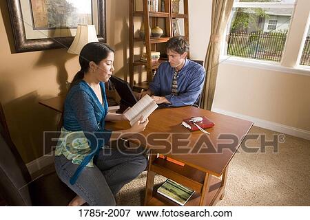 Stock Photo - Father using laptop computer at home while his teenage daughter reads a book. Fotosearch