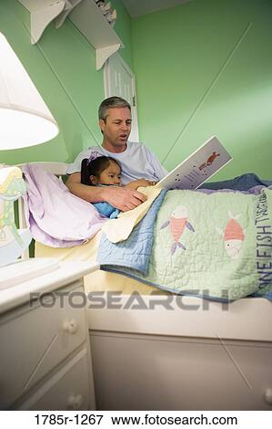 Stock Photo - Father with daughter reading book in bedroom. Fotosearch