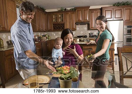 Stock Image - Girl and father serving dinner to their surprised Asian mother. Fotosearch