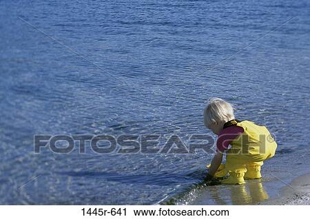 Stock Image - Girl bending down at the water's edge. Fotosearch