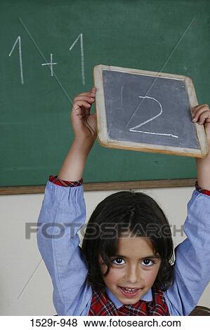 Stock Photo - Girl holding a chalkboard above her head in a classroom. Fotosearch
