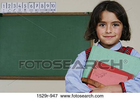 Girl standing in a classroom and holding books View Large Photo Image Stock Photo - Girl standing in a classroom and holding books. Fotosearch