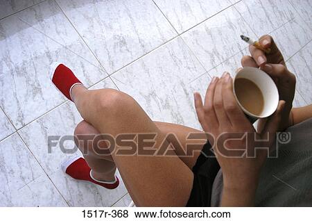 Stock Photo - High angle view of a young woman drinking tea and smoking a cigarette. Fotosearch