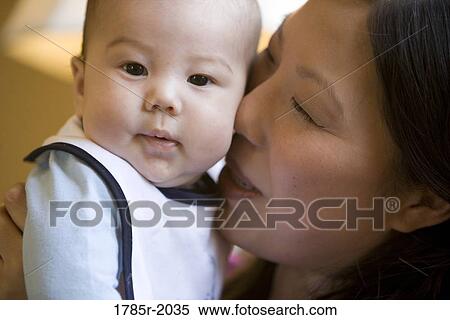 Stock Photography - Infant boy being kissed on the cheek by his mother. Fotosearch