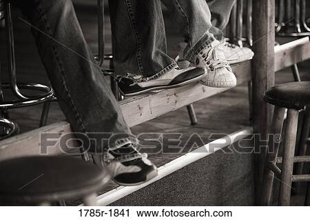 Stock Image - Legs of people sitting on bar stools. Fotosearch