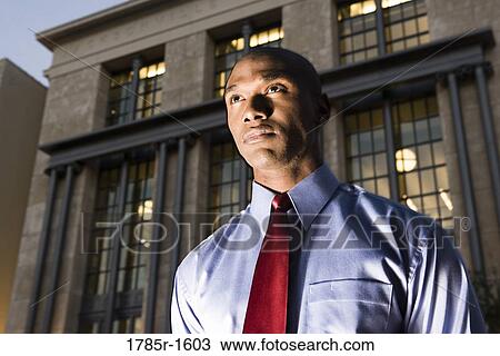 Low angle view of a young businessman at dusk, with building in background View Large Photo Image Stock Image - Low angle view of a young businessman at dusk, with building in background. Fotosearch