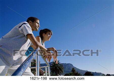 Low angle view of a young couple leaning against a railing View Large Photo Image Stock Photo - Low angle view of a young couple leaning against a railing. Fotosearch