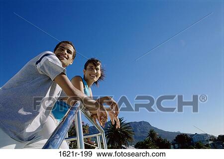 Stock Photo - Low angle view of a young couple leaning against a railing. Fotosearch