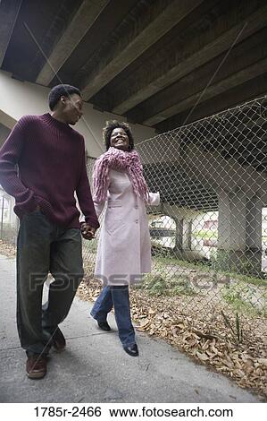 Stock Photograph - Low angle view of a young couple walking under a highway overpass. Fotosearch