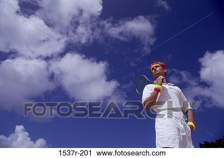 Stock Image - Low angle view of a young man holding a tennis racket. Fotosearch