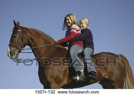 Low angle view of two girls on horseback View Large Photo Image Stock Image - Low angle view of two girls on horseback. Fotosearch