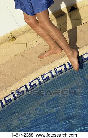 Stock Photo - Low section view of a person's legs dipping their toe into a swimming pool. Fotosearch