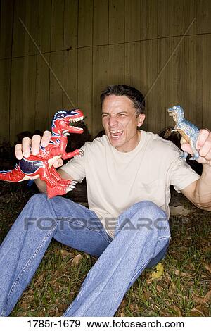 Stock Photo - Man playing with toy dinosaurs. Fotosearch