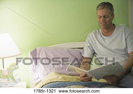 Stock Image - Man reading book in child's bedroom. Fotosearch
