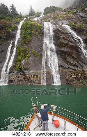 Stock Image - Man taking a picture of waterfalls from a boat, Endicott Arm, Alaska, USA. Fotosearch