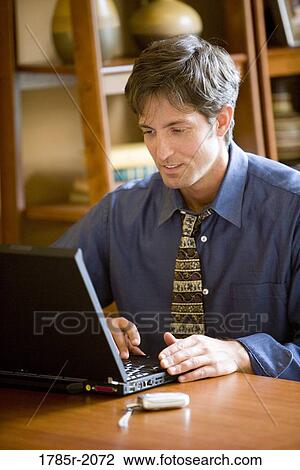 Stock Image - Man using laptop computer in the study of his home. Fotosearch
