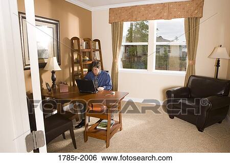 Stock Photograph - Man using laptop computer in the study of his home. Fotosearch