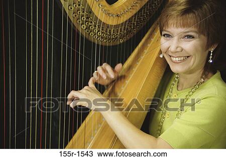 Mid adult woman playing the harp View Large Photo Image Stock Image - Mid adult woman playing the harp. Fotosearch