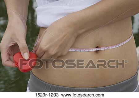 Mid section view of a woman measuring her waist View Large Photo Image Stock Image - Mid section view of a woman measuring her waist. Fotosearch