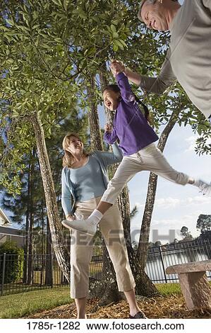 Stock Image - Mother and father playing with daughter in backyard. Fotosearch